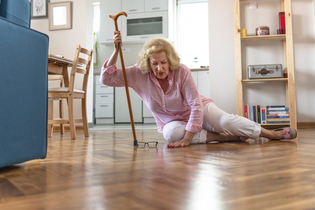 äldre kvinna som fallit i sitt hem, försöker resa sig med hjälp av käpp